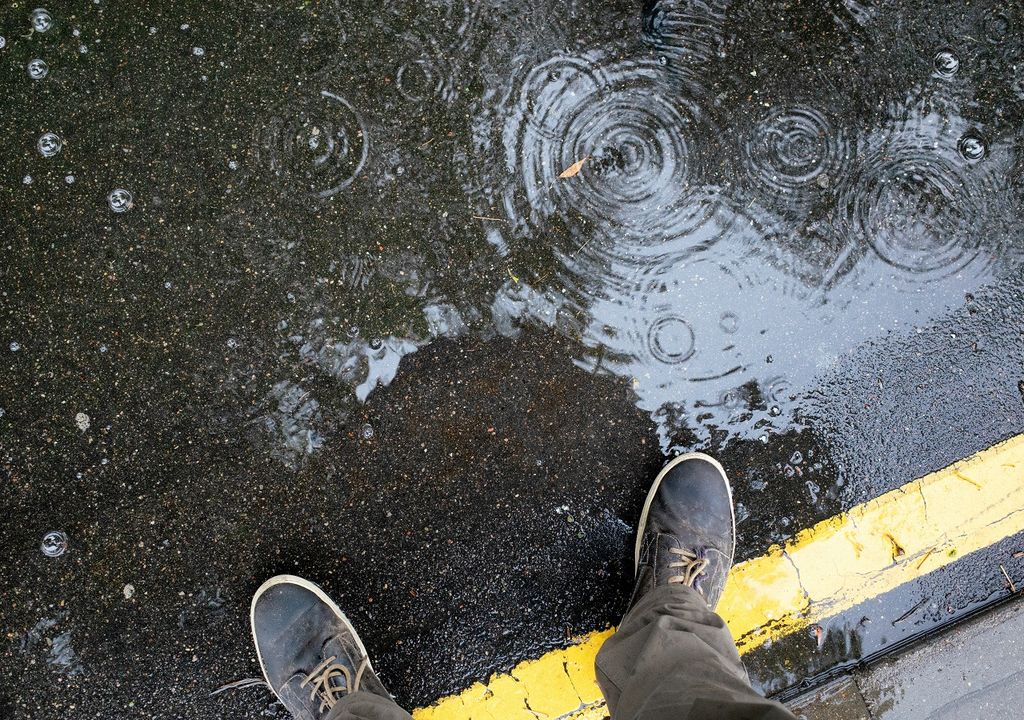 persona mirando su reflejo y las gotas de lluvia que caen en el suelo