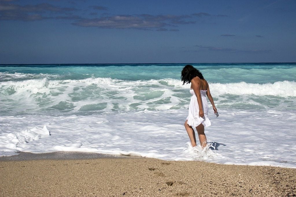 mujer vestida de blanco con los pies en el mar