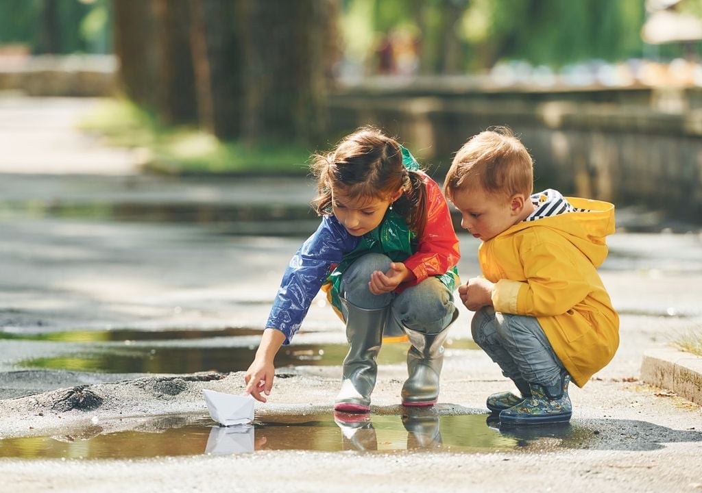 Niña y niño jugando en un charco de agua en una plaza