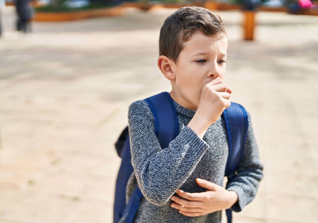 niño tosiendo en un parque, cargando una mochila