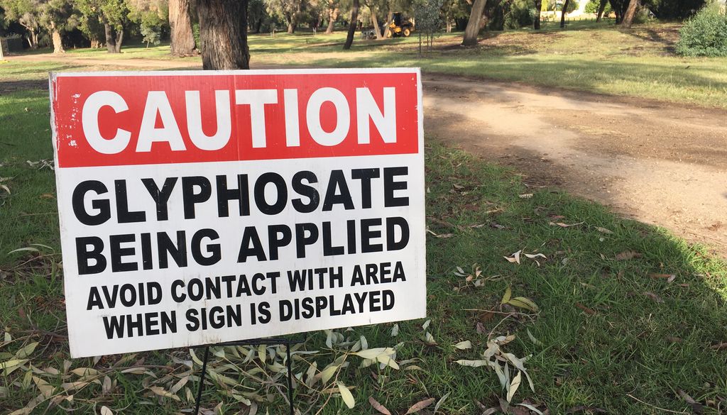 Cartel advirtiendo del peligro por fumigación con glifosato en un parque público.