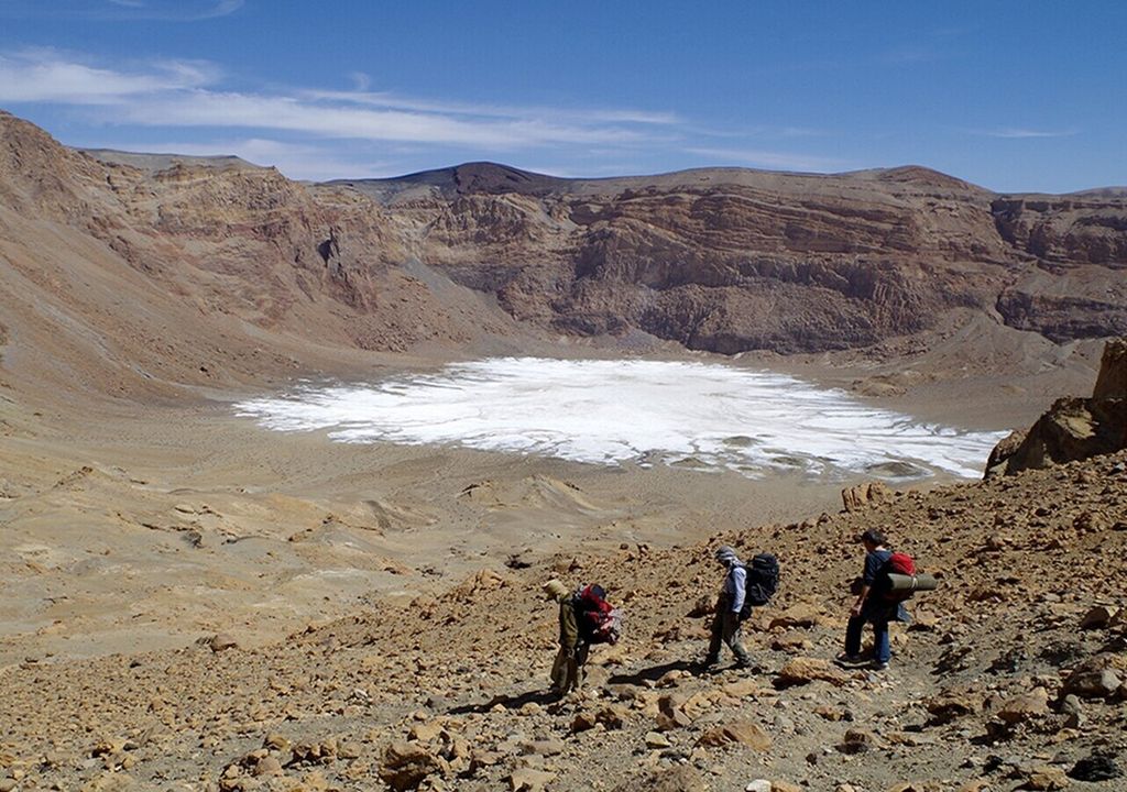 Abstieg in den Era-Kohor-Subkrater innerhalb der Gipfelcaldera des Emi Koussi – mit 3415 m der höchste Berg der Sahara. Auf dem Kraterboden liegen weißliche Sedimente: Die Salzkrusten sind Reste eines Paläosees, der den Krater einst teilweise füllte.