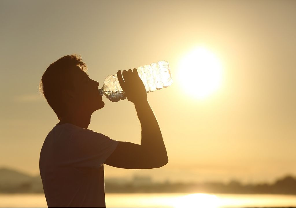 Hombre bebiendo agua con el sol de fondo