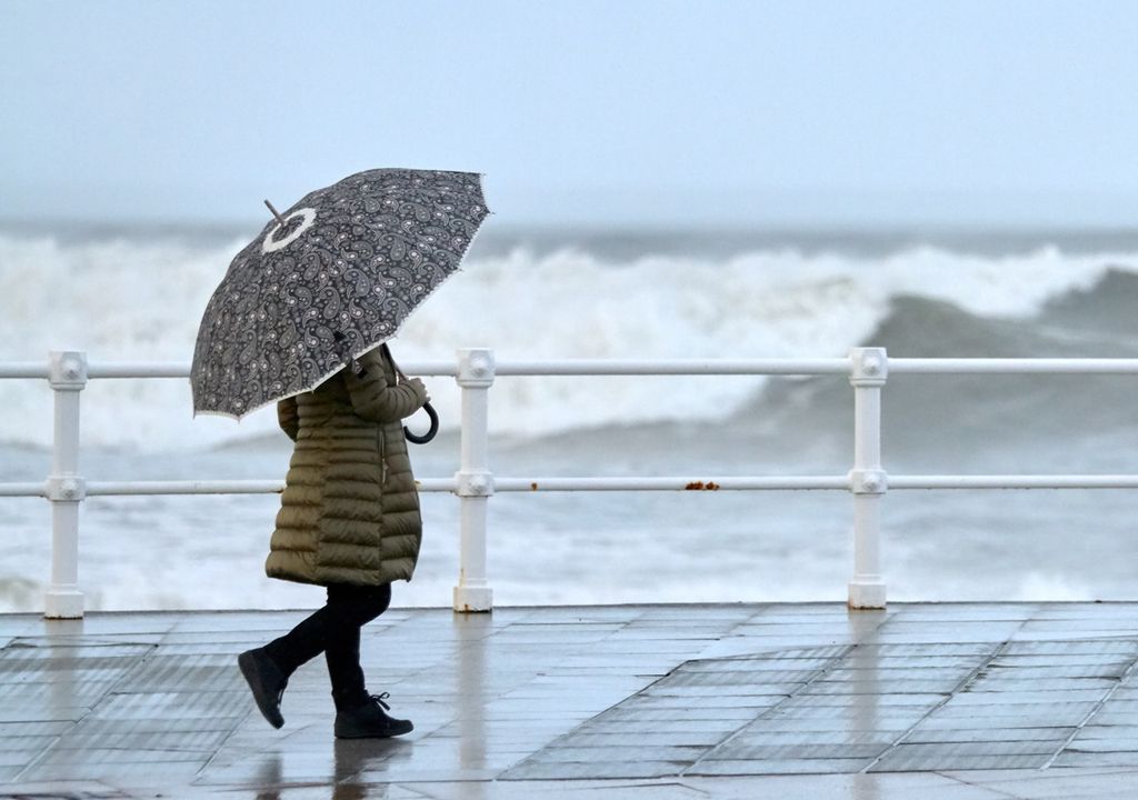 persona caminando en un día de lluvia, con paraguas, cerca del mar