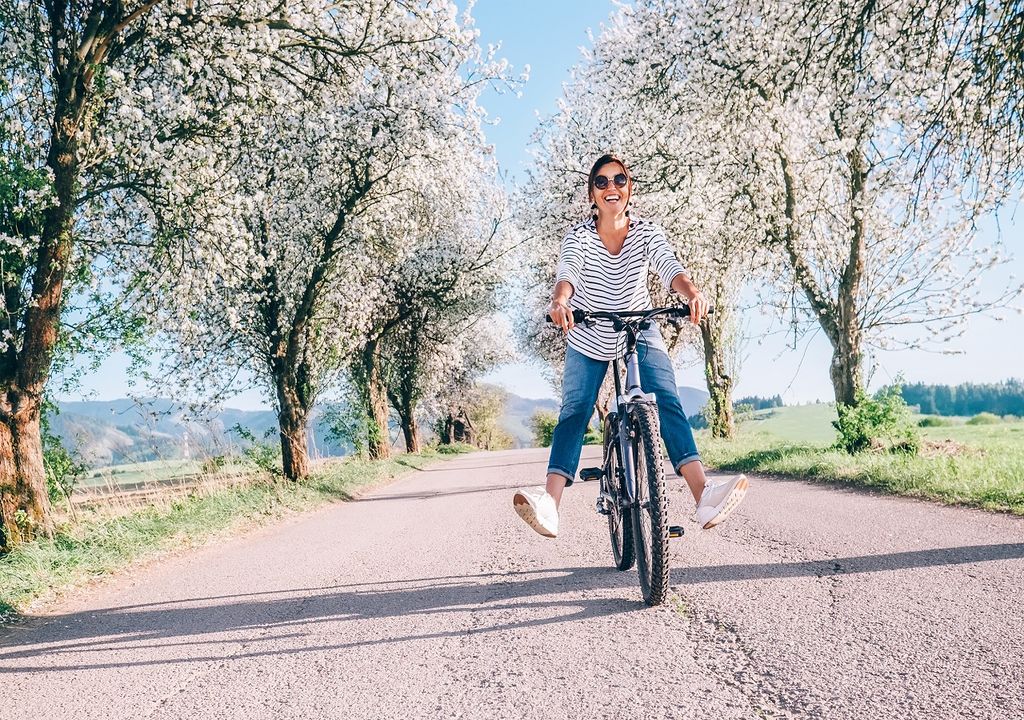Mujer en bicicleta, árboles con flores, camino