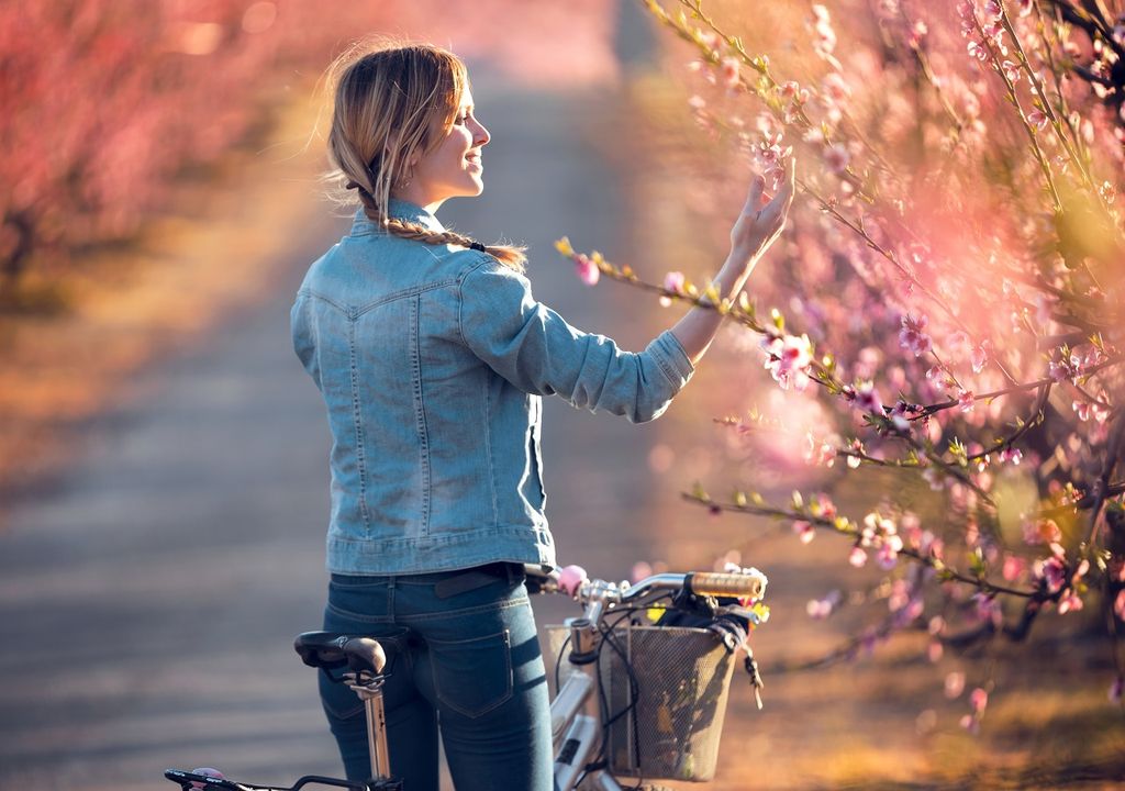 Mujer en bicicleta comtemplando las flores de los árboles
