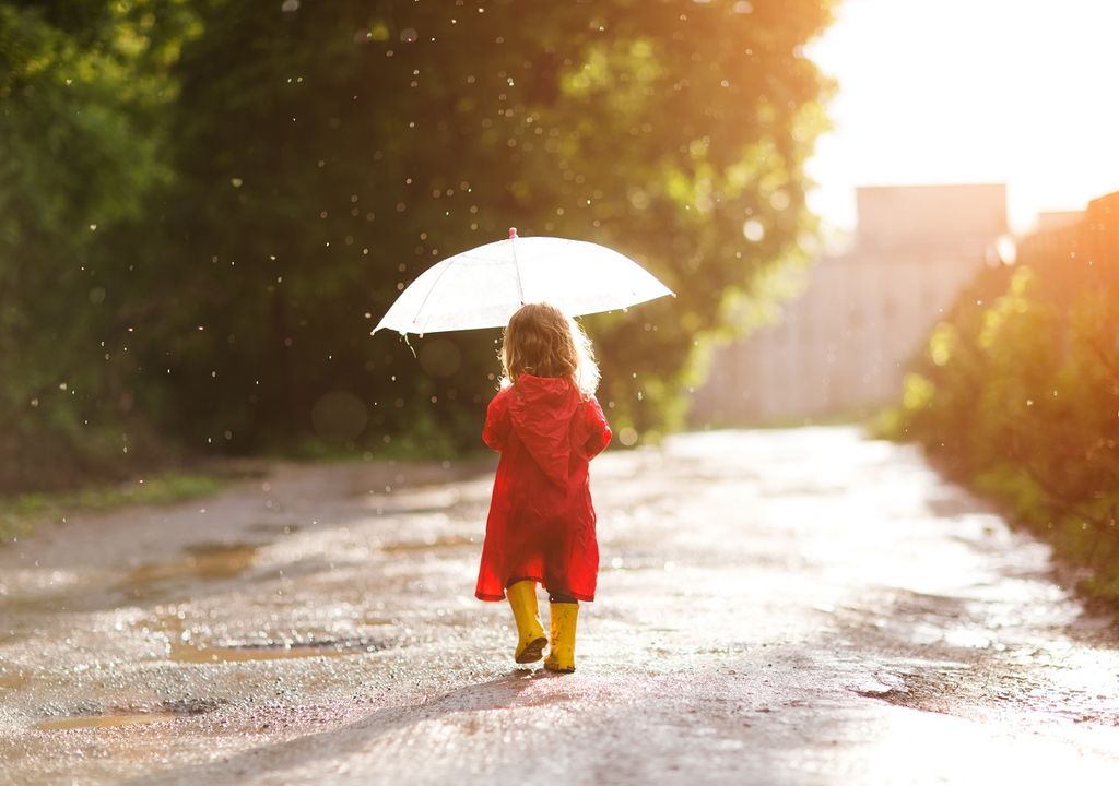 Niña de paragüas y botas caminando bajo lluvia suave