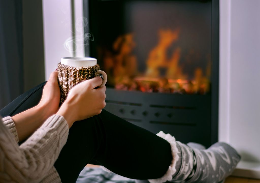 Mujer sentada frente al fuego con una taza en sus manos