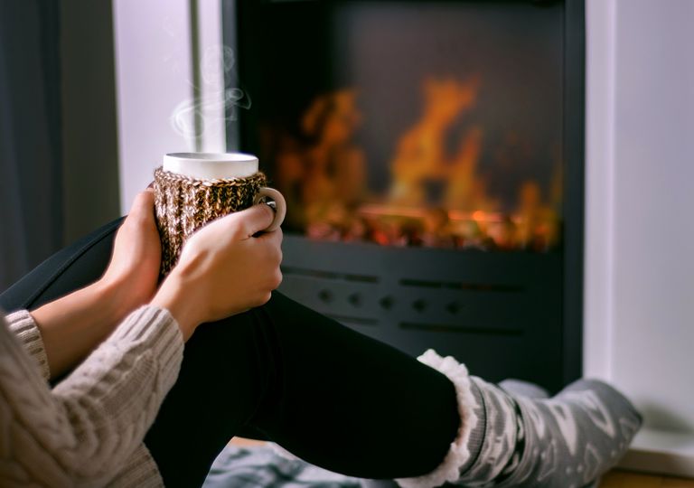 Mujer sentada frente al fuego con una taza en sus manos Mujer sentada frente al fuego con una taza en sus manos