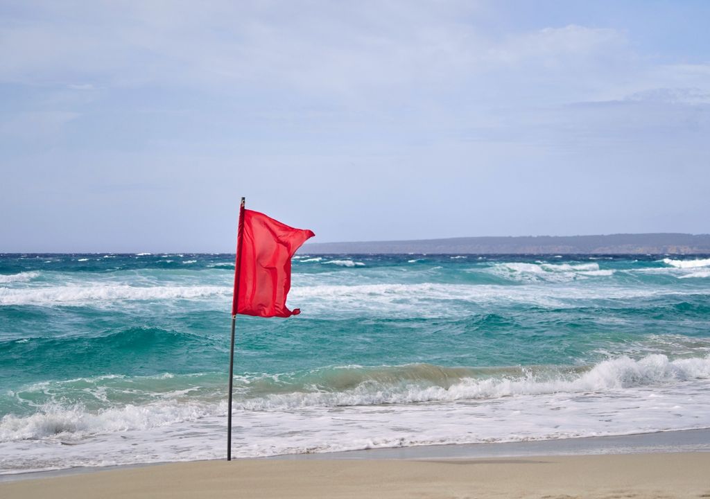 bandera roja flameando en una playa con oleaje intenso