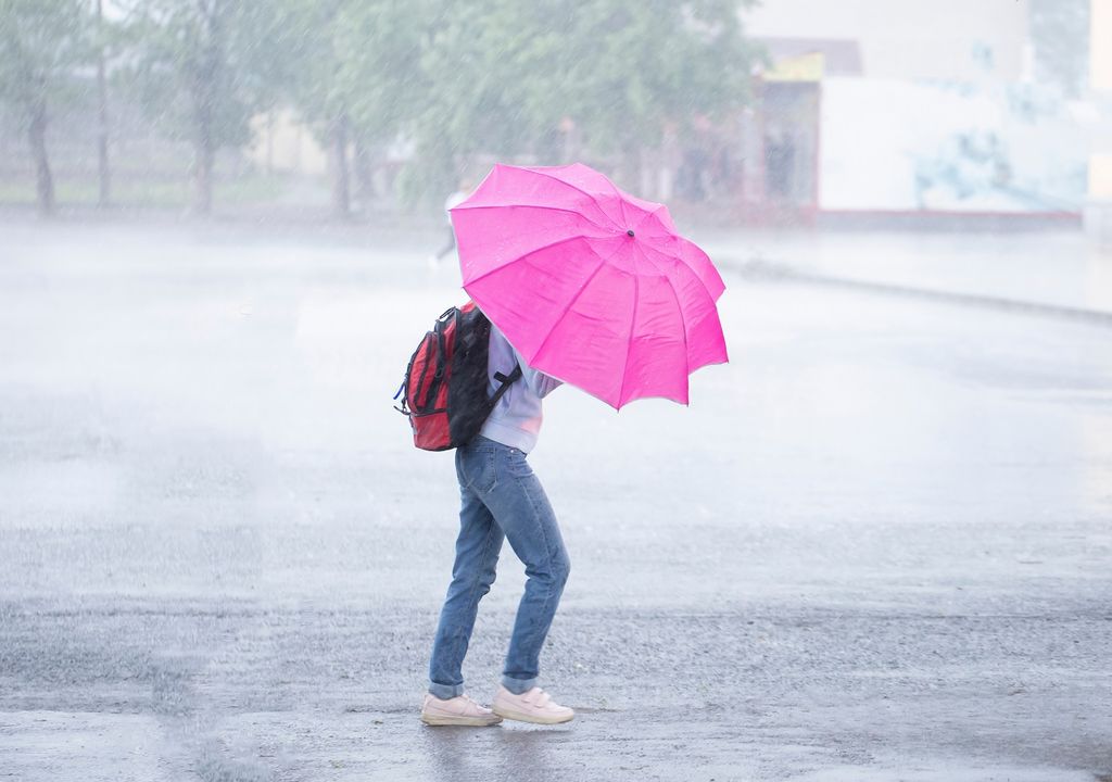 Persona con mochila bajo la lluvia con paraguas rosa fondo de lluvia intensa