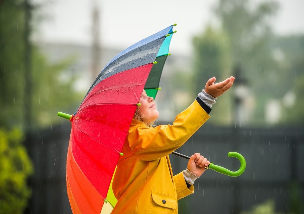 niña con paraguas extendiendo su mano para alcanzar las gotas de lluvia