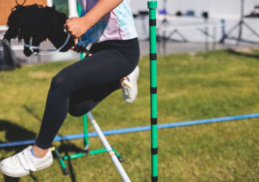 Hobby-Horse-Wettbewerb auf grünem Gras, Hobby-Pferdereiter, die springen, Training im Reitsport mit Steckenpferden.