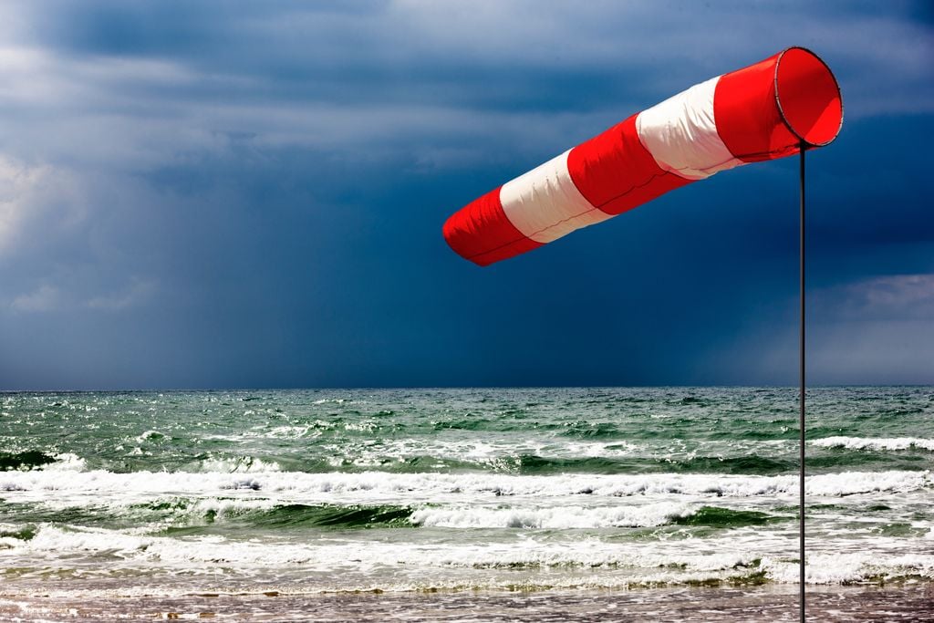 Durch ein Sturmtief aufgewühlte Nordsee, im Hintergrund ziehen dunkele Wolken und Regenschauer vorbei, während im Vordergrund der Wind den Windsack aufbläst.