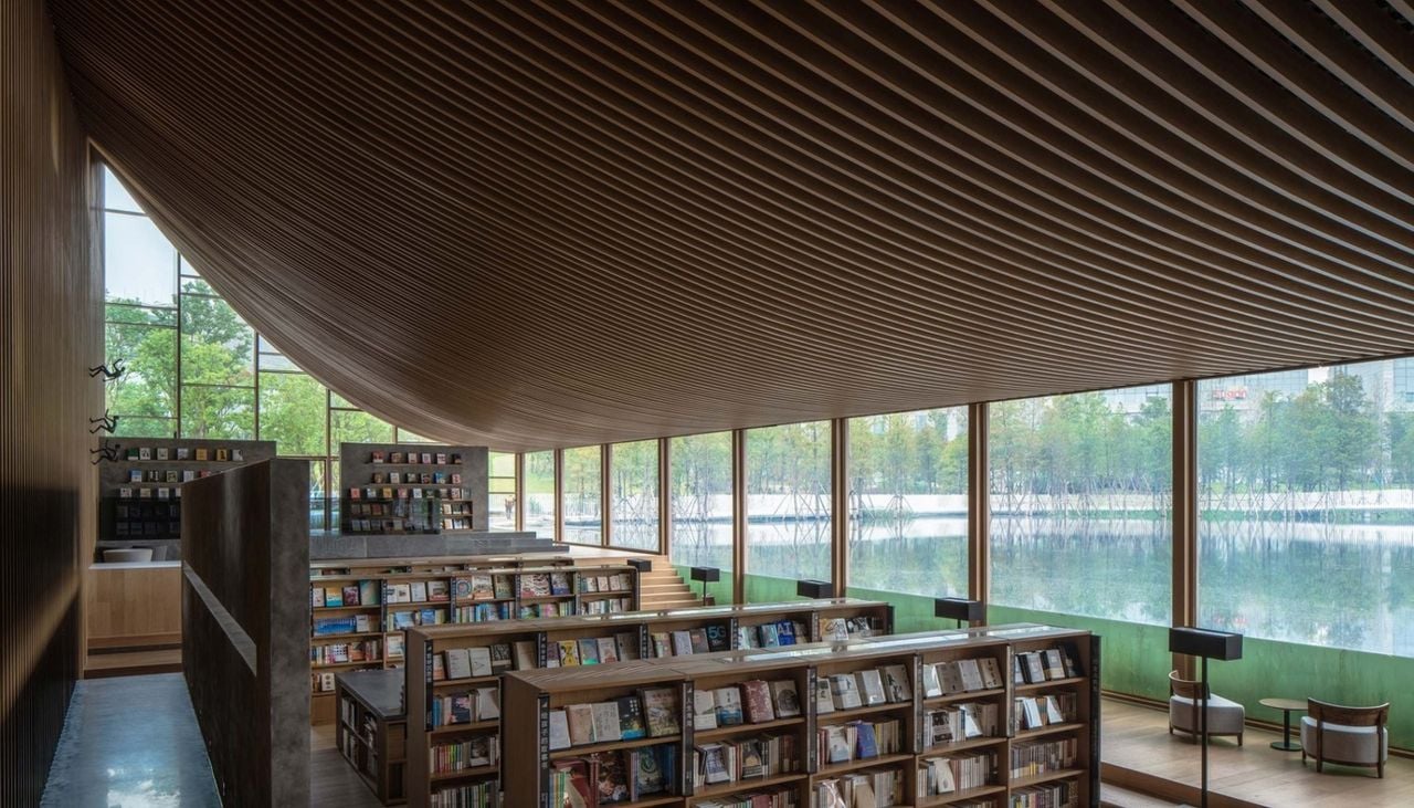Desde los ventanales inferiores, los visitantes pueden observar la vegetación lacustre y el nado de los peces mientras leen. Crédito: MUDA Architects y Arch Daily