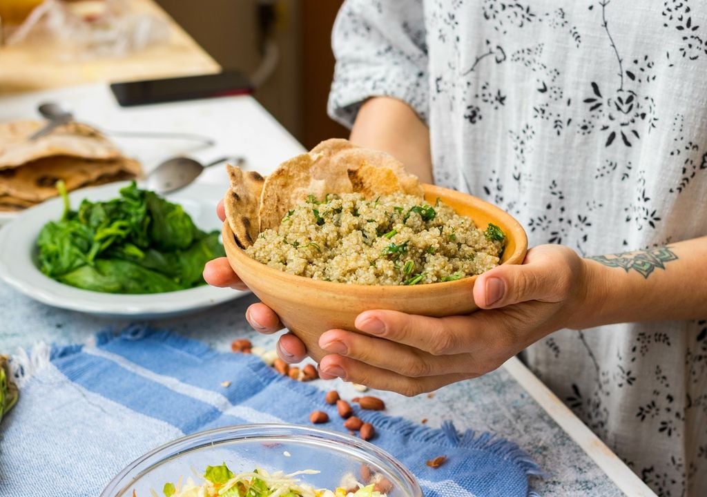 Salada de quinoa com ervas aromáticas nas mãos de uma mulher no fundo da cozinha