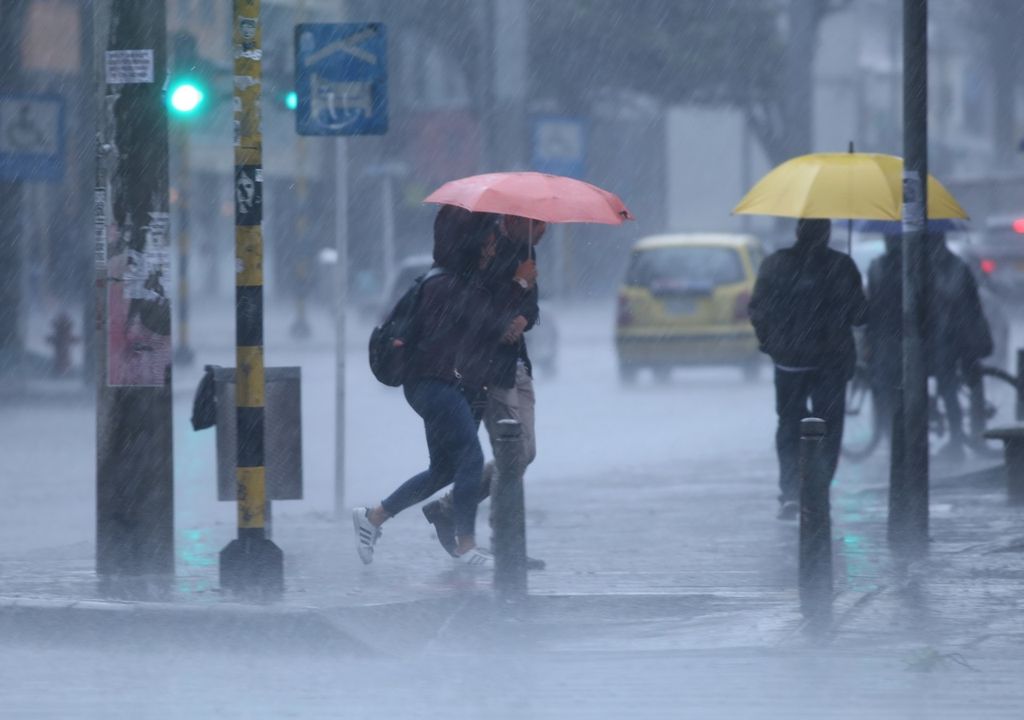 Personas con paraguas caminando bajo la lluvia, calles inundadas