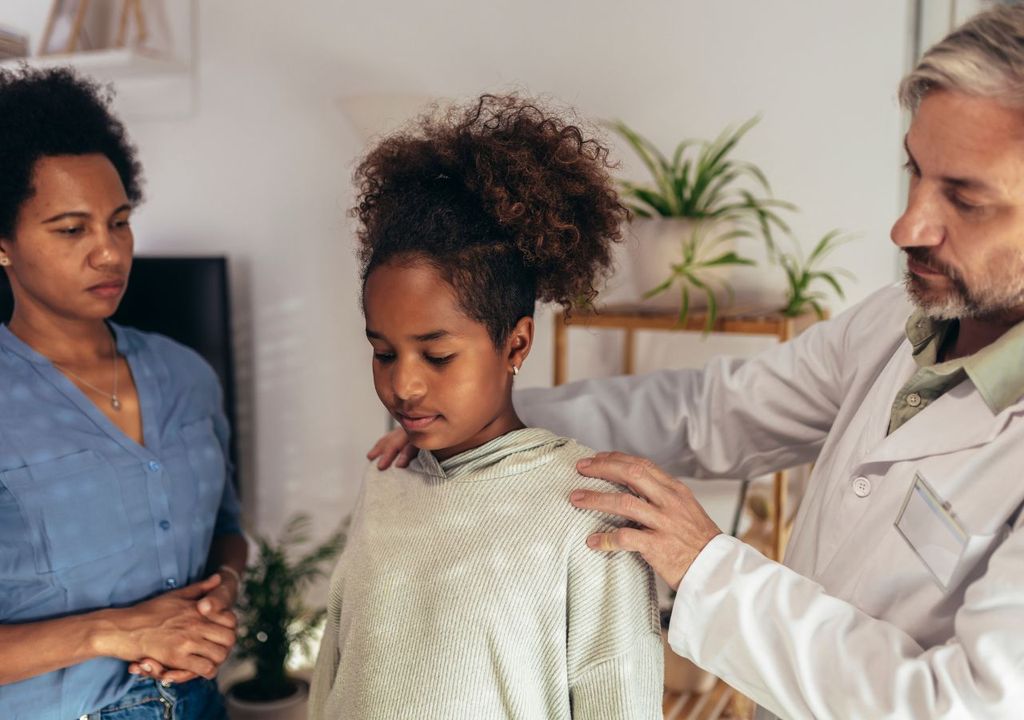 Niña con dolor de espalda acompañada por médico y enfermera en hospital