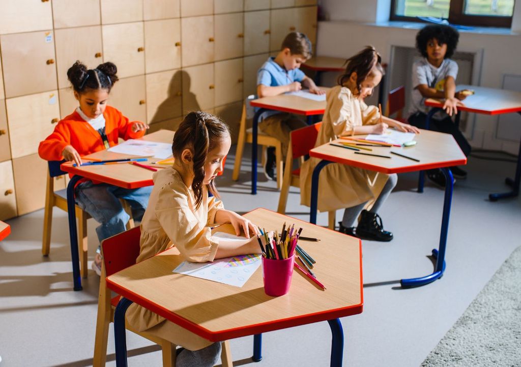 Cinco niños y niñas en sala de clases sentados en sus escritorios.