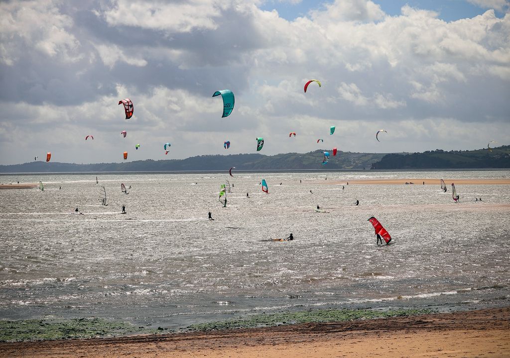 Cloudy, windy beach with windsurfers.