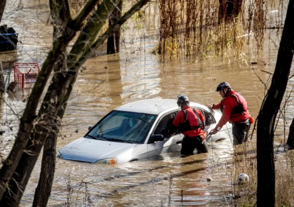 rescatistas ayudando una persona que está dentro de un vehículo aislado por el agua de las inundaciones