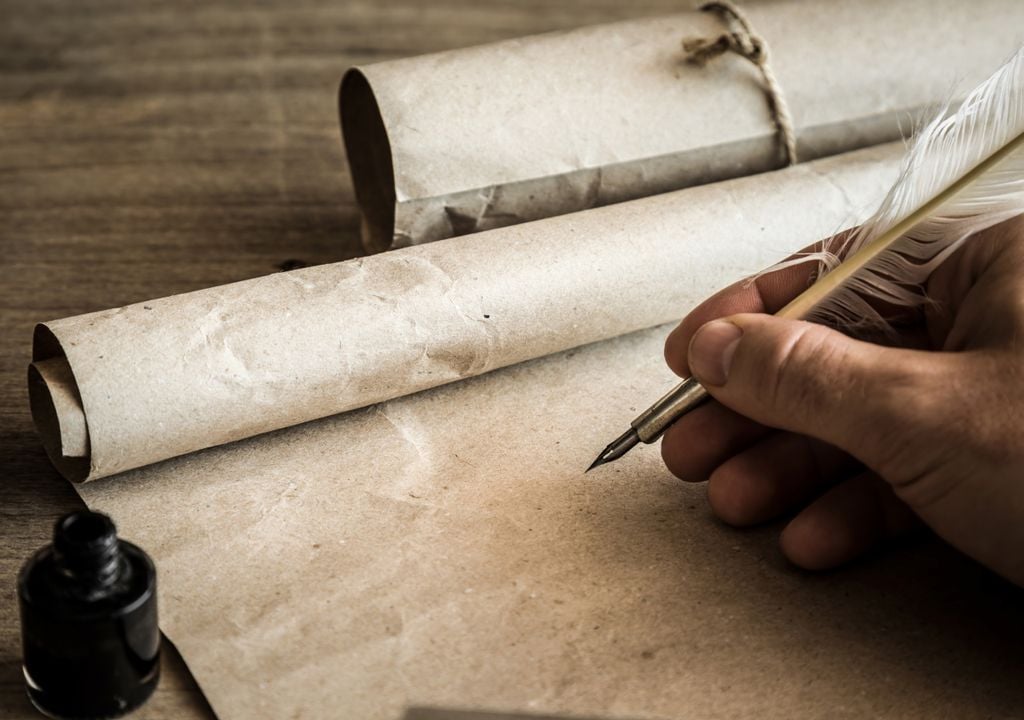 pergamino y una pluma para escribir afirmada por la mano de una persona