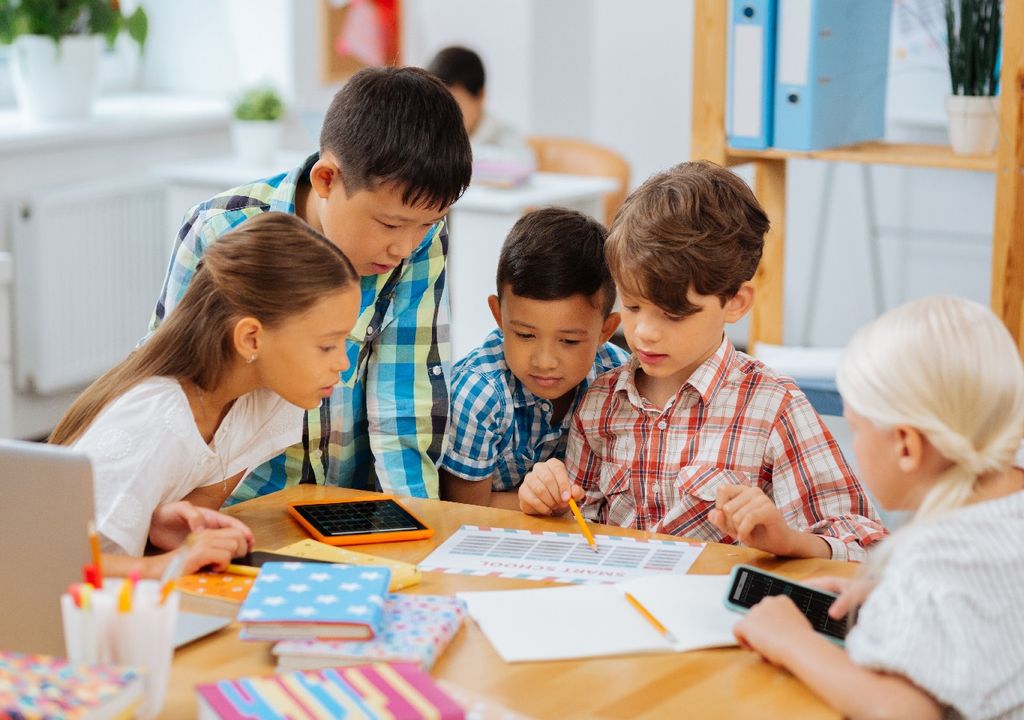 Niños mirando una hoja, mesa con lápices y cuadernos, fondo sala de clases Niños mirando una hoja, mesa con lápices y cuadernos, fondo sala de clases