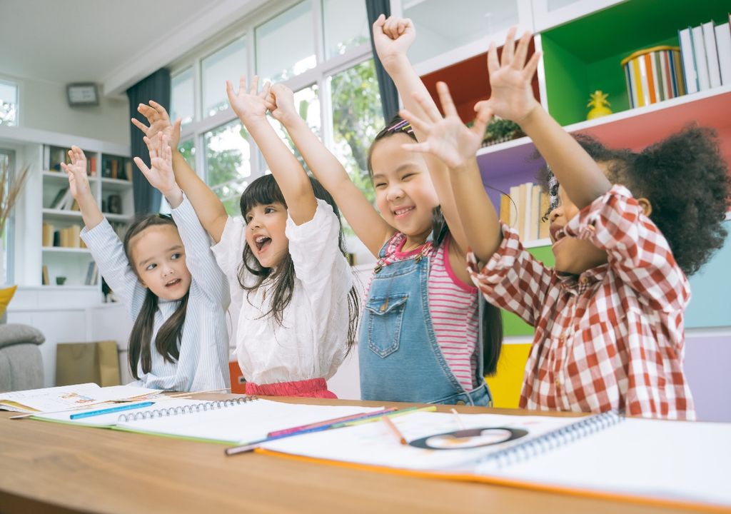 Niñas con las manos levantadas sonriendo en sala de clases Niñas con las manos levantadas sonriendo en sala de clases