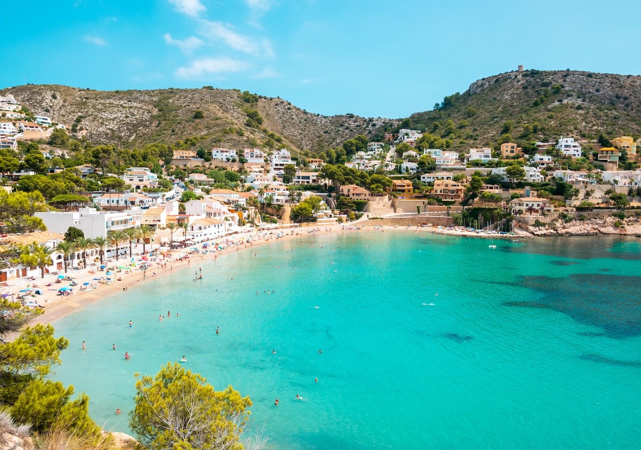 Vue de la plage d’El Portet de Moraira, un rivage de 300 mètres de long qui allie sable fin et recoins rocheux dans un environnement semi-urbain.
