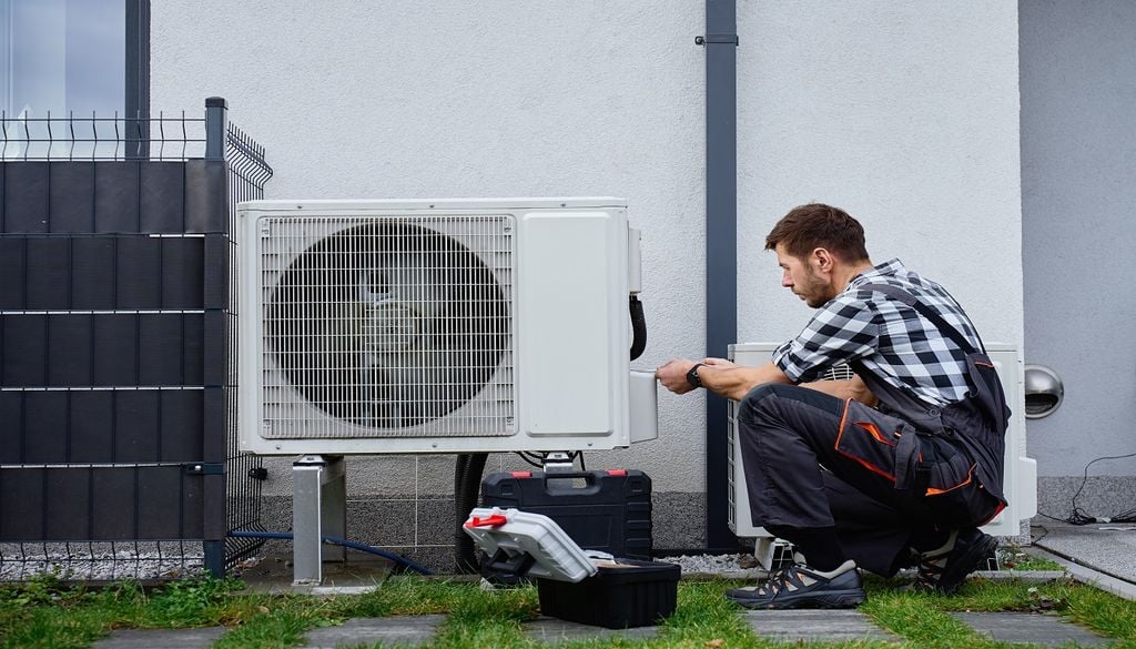 Técnico conserta aparelho de ar condicionado no exterior de um edifício Os gases fluorados usados nos aparelhos de ar condicionado possuem um impacto ambiental milhares de vezes superior ao CO2. Foto: Adobe Stock