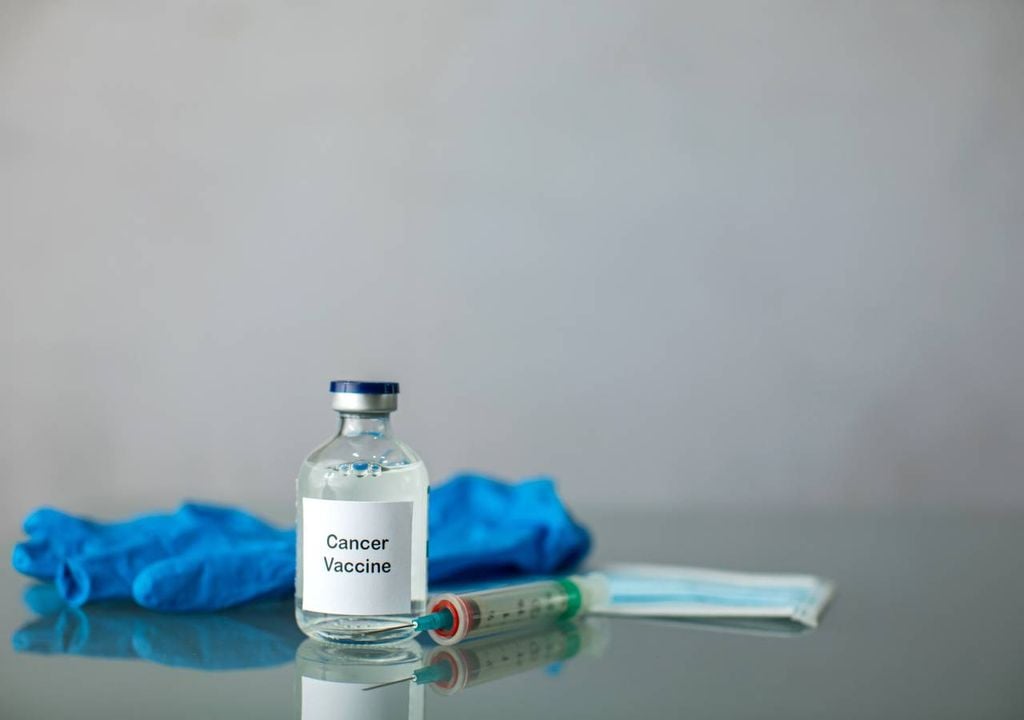 aguja, guantes, y botella con vacuna contra el cáncer, en una imagen referencial