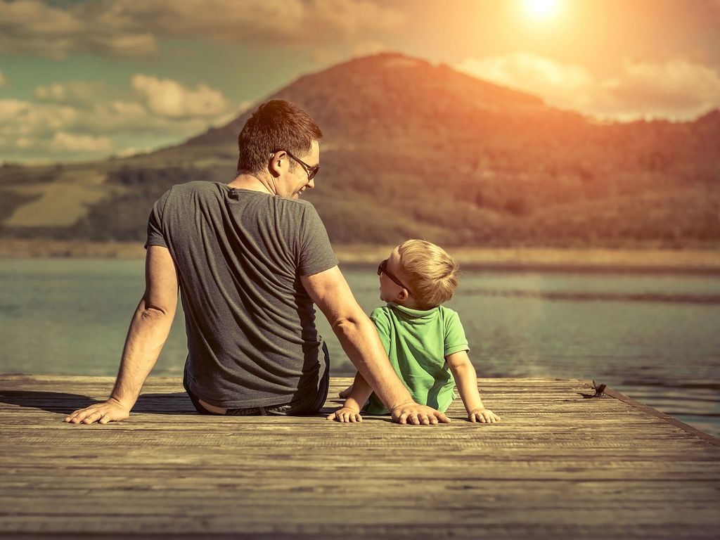 hijo y padre sentados cerca del lago