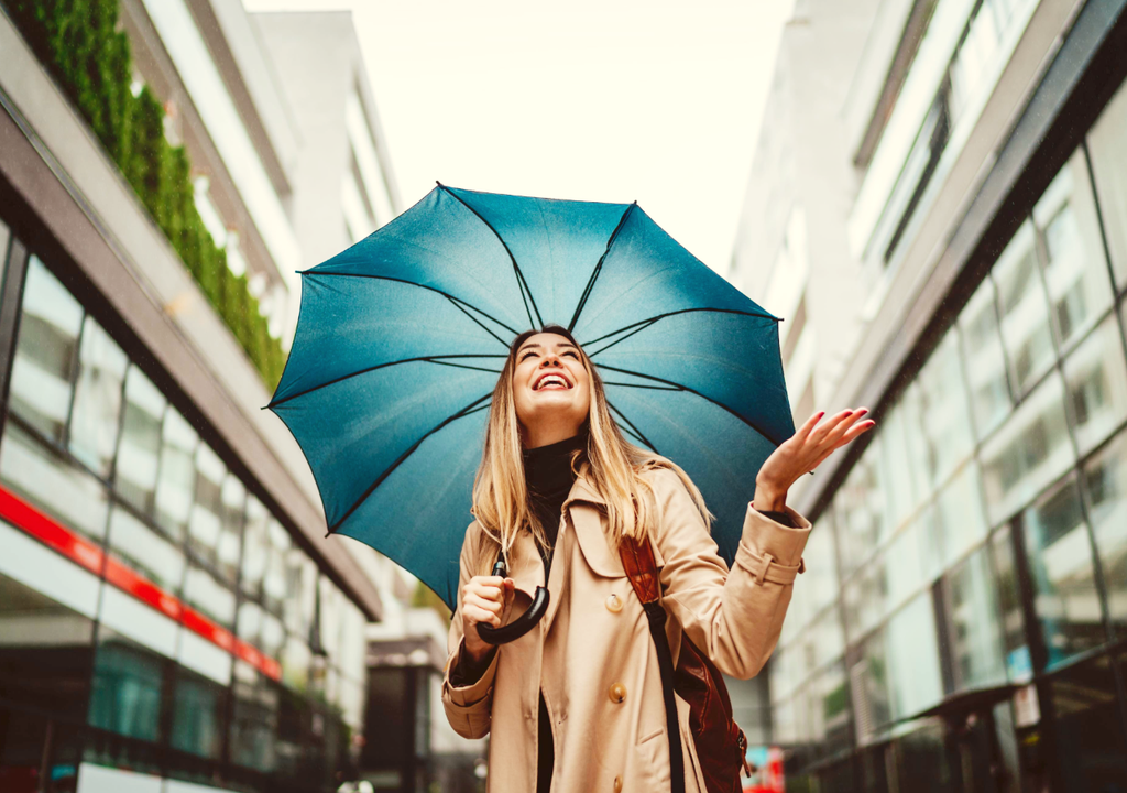 persona con la mano extendida hacia el cielo, cubierta por un paraguas, esperando por lluvias