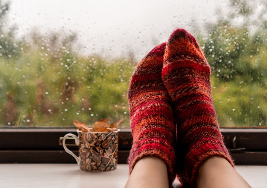 Pies con medias apoyados en la ventana. Día de lluvia de otoño