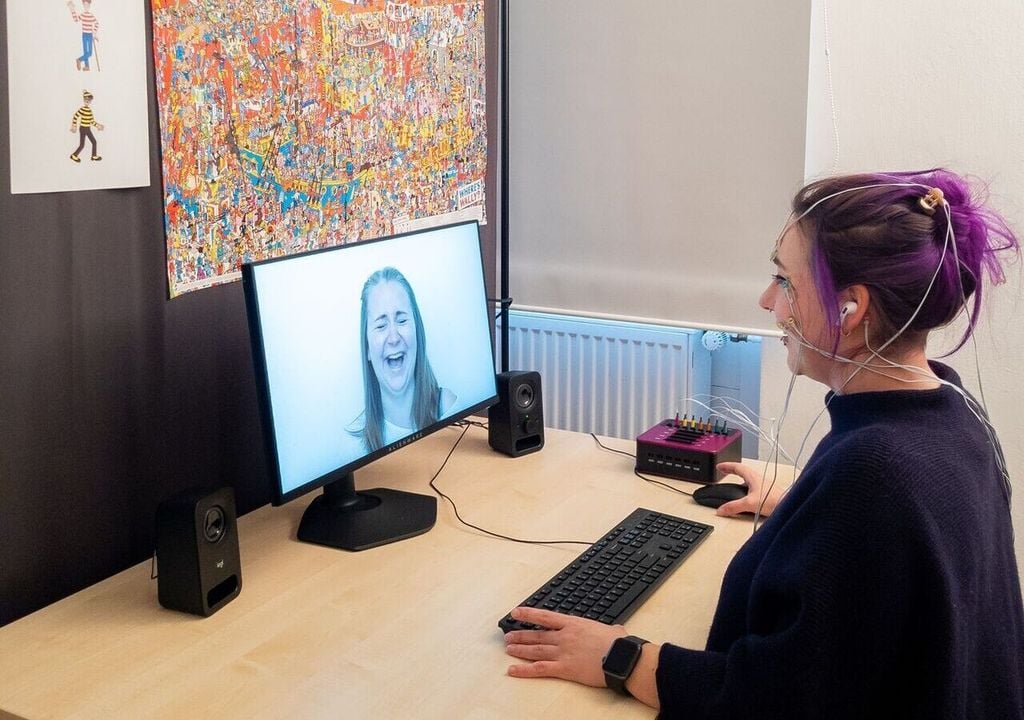 Versuchsperson im Experiment: Elektroden auf der Haut messen die Aktivitäten der Gesichtsmuskeln. Das bunte Suchbild soll vom Witz ablenken. Unmittelbar nach jedem Witz sah und hörte die Versuchsperson einen lachenden Menschen. Versuchsperson im Experiment: Elektroden auf der Haut messen die Aktivitäten der Gesichtsmuskeln. Das bunte Suchbild soll vom Witz ablenken. Unmittelbar nach jedem Witz sah und hörte die Versuchsperson einen lachenden Menschen.