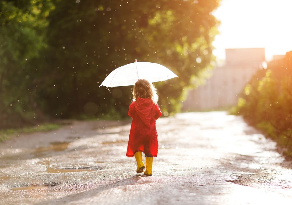Niña caminando con un paragua bajo cielo parcial y lluvia
