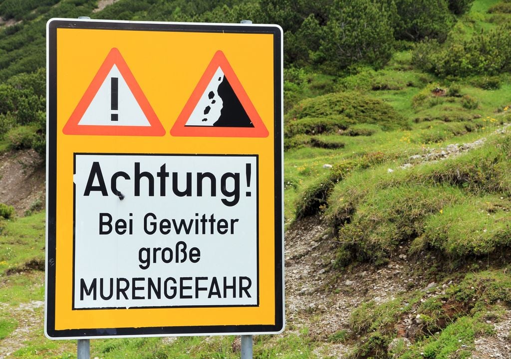 Hinweisschild in den Alpen, dass vor der Gefahr von Murenabgängen bei Gewitter warnt.