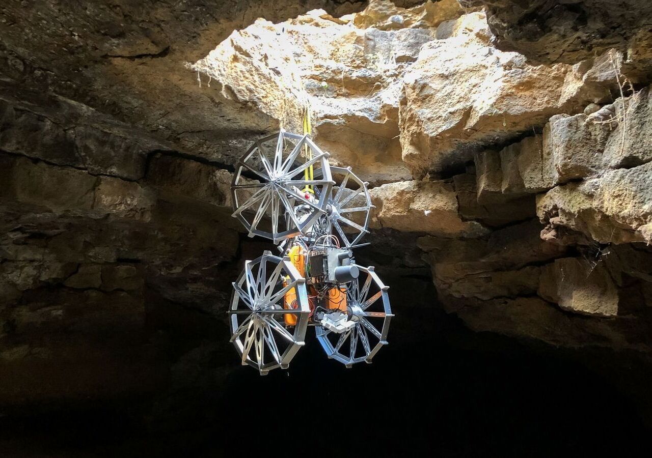 Kooperative robotergestützte Erkundung einer planetarischen Oberflächenöffnung und einer Lavahöhle: Coyote III seilt sich mithilfe eines von SherpaTT bereitgestellten Abseil- und Dockingsystems in die Höhle ab. Bild: DFKI/Tom Becker